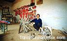 The smiling woman is spinning thread with an old spinning wheel in a Shaanxi local residence.