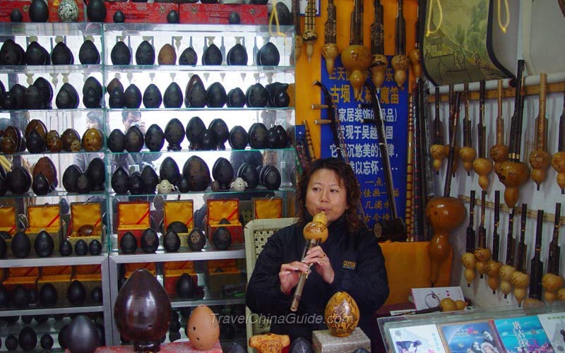 The shop owner is performing traditional Chinese music with the musical instrument Hulusi.